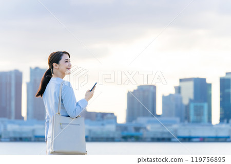 一個在城市背景下拿著智能手機的女人 一個在城市背景下拿著智能手機的女人 119756895