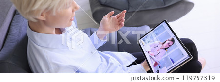 Blonde woman talks with doctor on video call via gadget 119757319