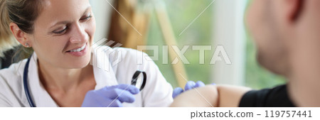 Dermatologist with magnifying glass examines patient arm 119757441