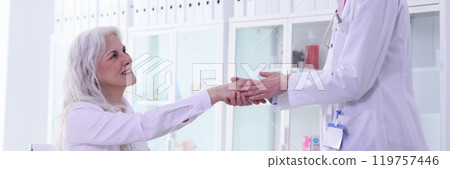 Positive blonde doctor greets with handshake mature woman Positive blonde doctor greets with handshake mature woman 119757446