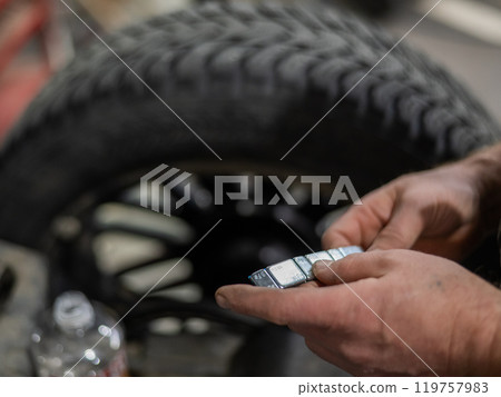 A mechanic attaches balancing weights to a wheel.  119757983