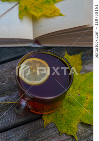 glass cup of hot tea with lemon with maple leaves and open book on wooden floor. High quality photo 119758161