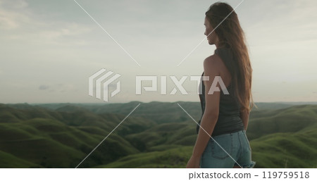 A woman stands atop a vibrant green hillside on Wild Sumba Island in Indonesia, captured in . 119759518
