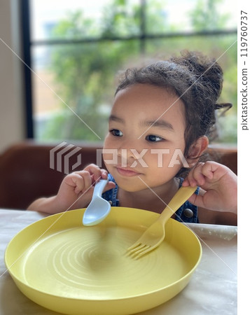 Portrait of a cute little girl eating with spoon and fork at home Portrait of a cute little girl eating with spoon and fork at home 119760737