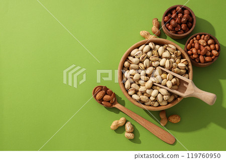 Different types of nuts in wooden bowls on a green background Different types of nuts in wooden bowls on a green background 119760950