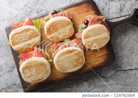 Italian tigelle or Crescentina modenese with sausage, jamon and fresh vegetables close-up on a wooden board. Horizontal top view 119762009
