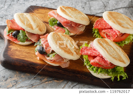 Small italian tigelle sandwiches with sausage, jamon and fresh vegetables close-up on wooden board. Horizontal 119762017