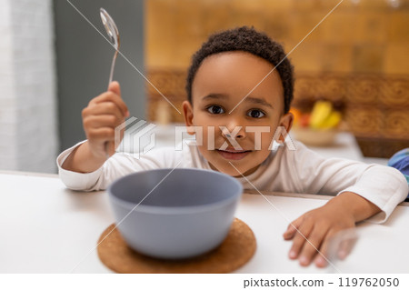 Dark-skinned boy sitting at the table and eating cereals 119762050