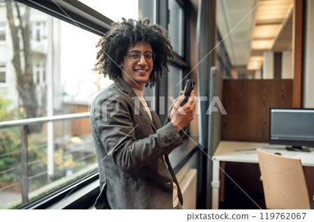 Smiling young man near the window with a phone in hands 119762067