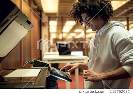 Curly-haired young man making copies on xerox in the library 119762085