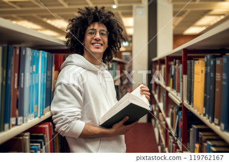 Dark-haired young guy standing near the bookshelves and reading a book 119762167