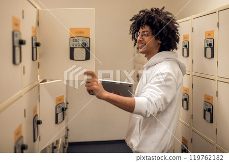 Curly-haired young guy standing near the lockers in library archive Curly-haired young guy standing near the lockers in library archive 119762182