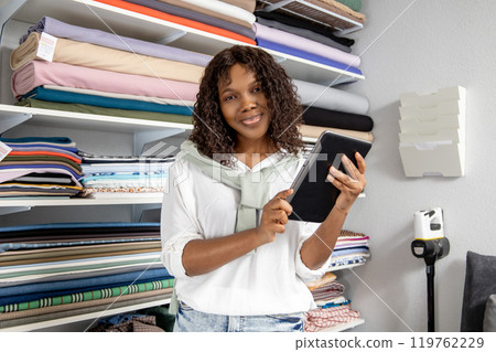 Female dressmaker in retail store choosing fabric using tablet to check stock place orders online Female dressmaker in retail store choosing fabric using tablet to check stock place orders online 119762229