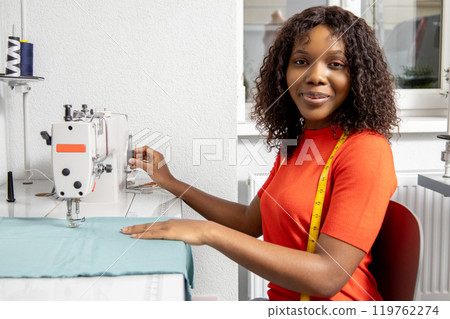 African american dressmaker sitting at the sewing machine and looking contented 119762274
