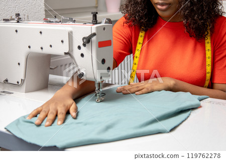 African american dressmaker sitting at the sewing machine and looking contented African american dressmaker sitting at the sewing machine and looking contented 119762278