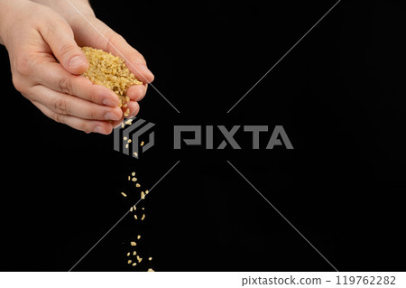 Hands pouring raw uncooked bulgur cereals on a black background space for text 119762282