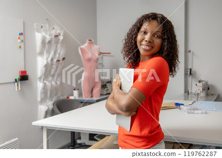 Curly-haired african american seamstress working in her studio Curly-haired african american seamstress working in her studio 119762287