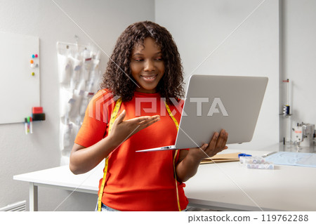 African american young seamstress with a laptop discussing something on the phone African american young seamstress with a laptop discussing something on the phone 119762288