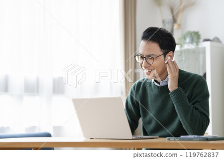 一名 30 多歲的男子戴著耳機用筆記型電腦進行視訊通話 119762837