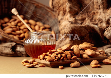 Almond nuts in a wooden dish and honey in a glass jar. 119763230