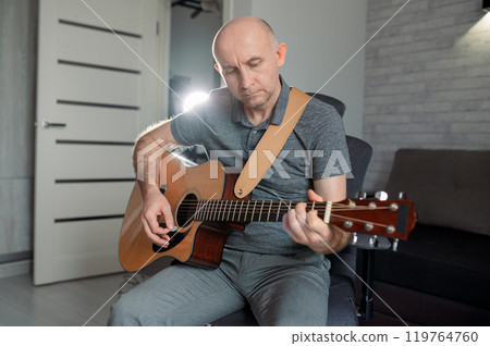 Guitarist paying a acoustic guitar in office. portrait Male musician sitting on sofa and playing music instrument 119764760