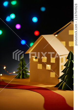 Christmas-themed vertical image on the dark backdrop, decorated by paper houses and pines wrapped in glowing LED lights, with a red paper roll across the surface, above which are colorful LED lights. Christmas-themed vertical image on the dark backdrop, decorated by paper houses and pines wrapped in glowing LED lights, with a red paper roll across the surface, above which are colorful LED lights. 119764928