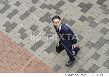 一位中年商人在城市中行走，對著鏡頭微笑的俯視圖 119764996