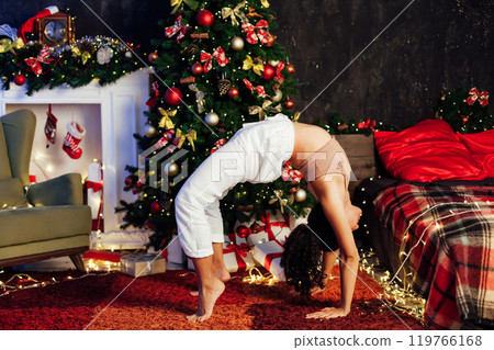 woman yoga gymnastics at Christmas tree with gifts for new year 119766168