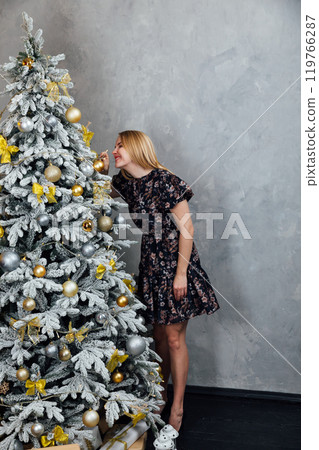 Blonde woman in dress smiling with gifts Christmas tree for new year 119766287