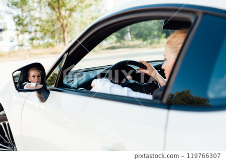 woman driver sitting behind the wheel of a white car on the road woman driver sitting behind the wheel of a white car on the road 119766307