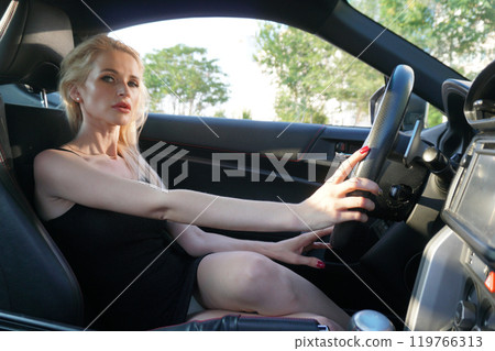woman driver in black dress sitting behind the wheel of a car 119766313