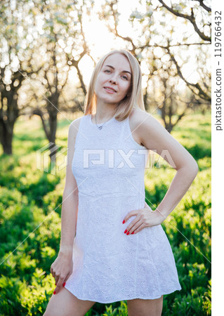 Beautiful blonde woman in summer dress walking in the garden of flowering trees Beautiful blonde woman in summer dress walking in the garden of flowering trees 119766432