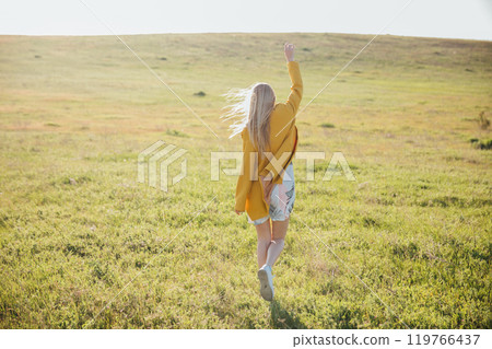 Beautiful blonde woman in summer dress walking in blooming field at sunset Beautiful blonde woman in summer dress walking in blooming field at sunset 119766437