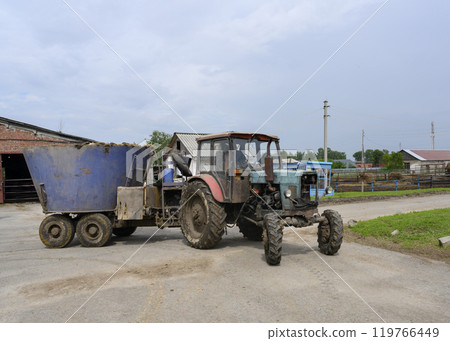 A tractor delivers food around the farm while the cows are out for a walk A tractor delivers food around the farm while the cows are out for a walk 119766449