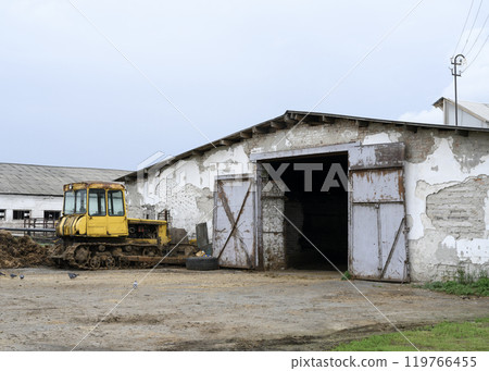 An old yellow tractor in front of a farm building built seventy years ago An old yellow tractor in front of a farm building built seventy years ago 119766455