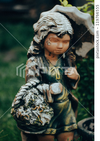 Worn stone angel. Vintage female figurine with shabby paint on her face. Monument in a cemetery. Old statue close up. Sadness, longing, depression. Worn stone angel. Vintage female figurine with shabby paint on her face. Monument in a cemetery. Old statue close up. Sadness, longing, depression. 119766555
