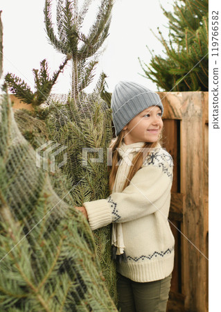 A girl chooses a Christmas tree in a shop A girl chooses a Christmas tree in a shop 119766582