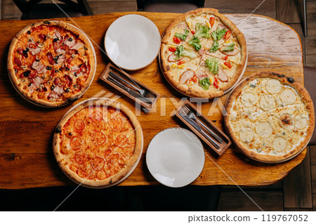 Assorted pizzas on a rustic wooden table, ready to serve with plates and cutlery 119767052