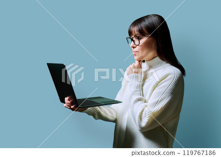 Serious middle aged woman using laptop on blue background 119767186