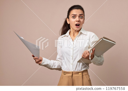 shocked surprised businesswoman in white shirt holding folders with documents on beige background 119767558
