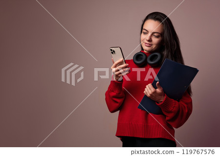 Happy girl wearing red sweater and headphones with folder and smartphone on dark background. 119767576