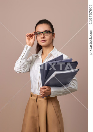 smiling businesswoman holding folders. Confident woman in glasses and white shirt looking at the camera 119767603
