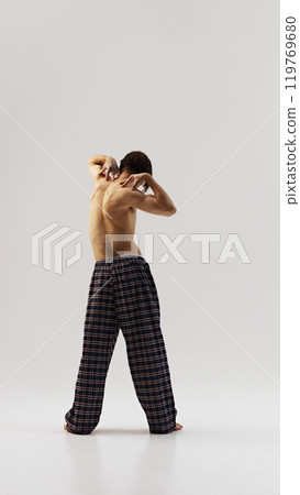 Rear view photo of bare-chested young man with toned body posing in plaid pants against white studio background. Muscled back. Rear view photo of bare-chested young man with toned body posing in plaid pants against white studio background. Muscled back. 119769680
