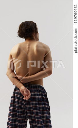Back view of young man in plaid pants with hands behind back against white studio background. Shows natural physique, relaxation, and wellness. Back view of young man in plaid pants with hands behind back against white studio background. Shows natural physique, relaxation, and wellness. 119769681