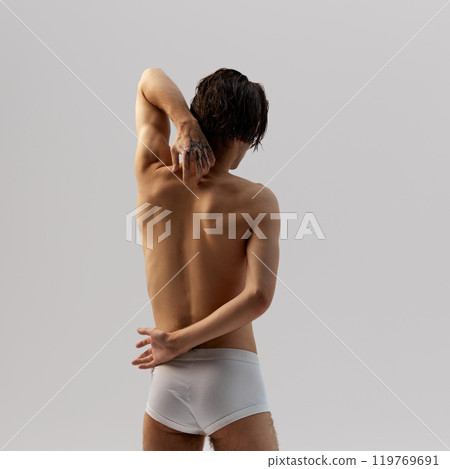 Rear view of young man with wet hair, relaxed posture, showcasing natural physique and masculine beauty against grey background. Rear view of young man with wet hair, relaxed posture, showcasing natural physique and masculine beauty against grey background. 119769691