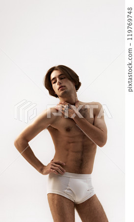 Portrait of young man posing gracefully, put hand on shoulder against white studio background. Male model posing in underwear. 119769748