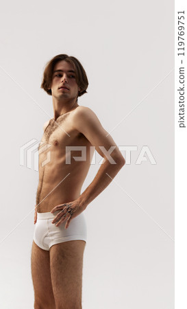 Young handsome man, posing in white underwear holding hands on hips and looking at distance seriously against white studio background. 119769751
