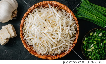 Fresh bean sprouts in a basket, accompanied by tofu, green onions, and garlic, ready for cooking. 119770340