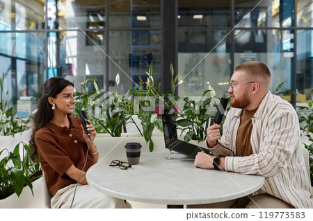 Side view of smiling man and woman engaged in pleasant conversation while recording podcast episode in cozy cafe with green plants, copy space Side view of smiling man and woman engaged in pleasant conversation while recording podcast episode in cozy cafe with green plants, copy space 119773583