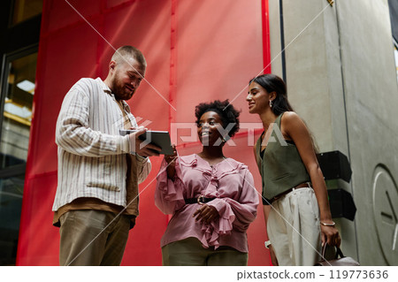 Medium shot of diverse group of three workers discussing business matters while looking at digital tablet screen during meeting in hallway of modern office center, copy space Medium shot of diverse group of three workers discussing business matters while looking at digital tablet screen during meeting in hallway of modern office center, copy space 119773636